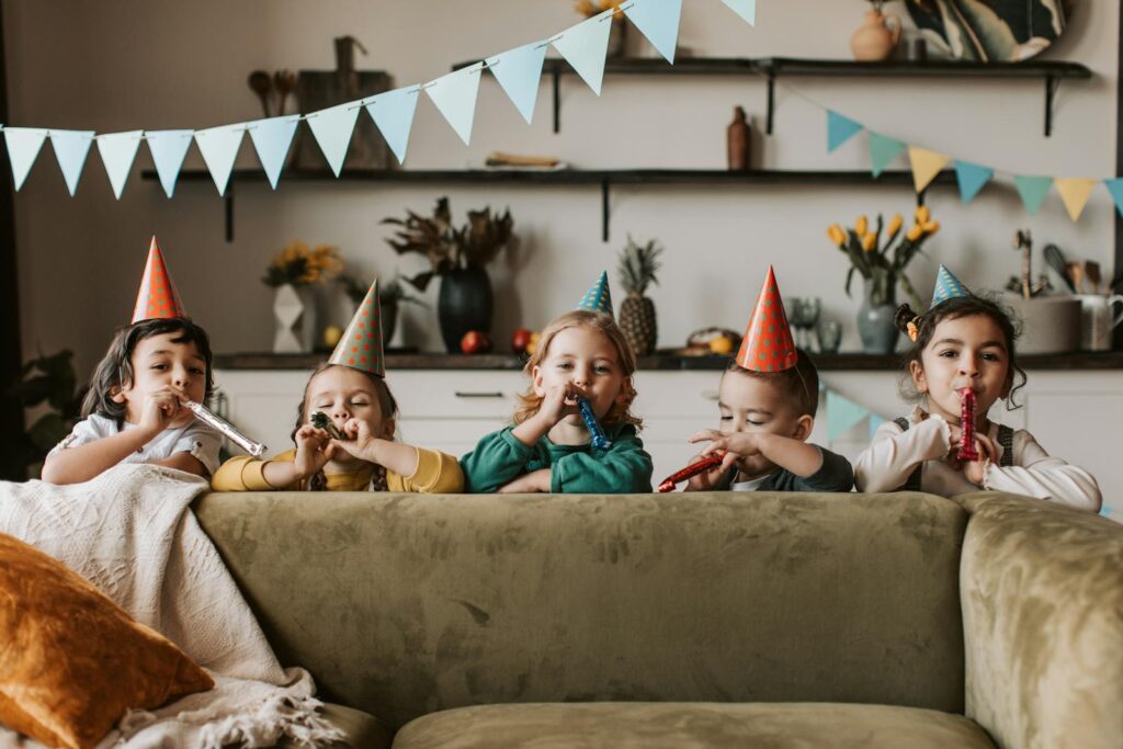 Group of children celebrating a birthday indoors with party hats and blowers.