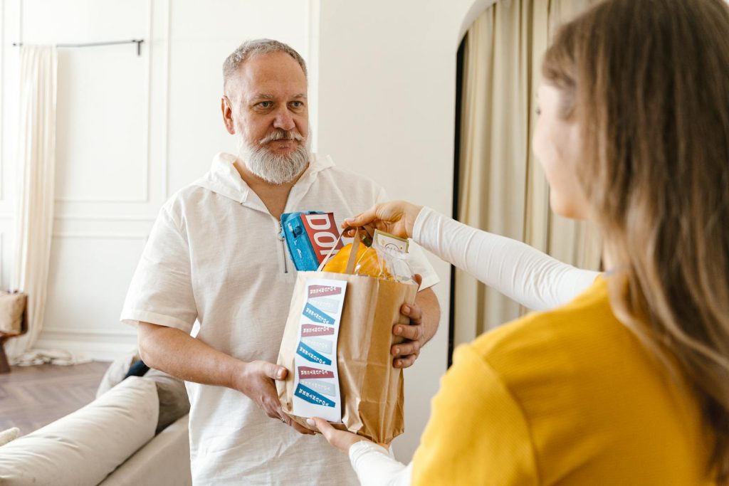 An elderly man with a beard receiving a donation in a paper bag indoors, highlighting community support.