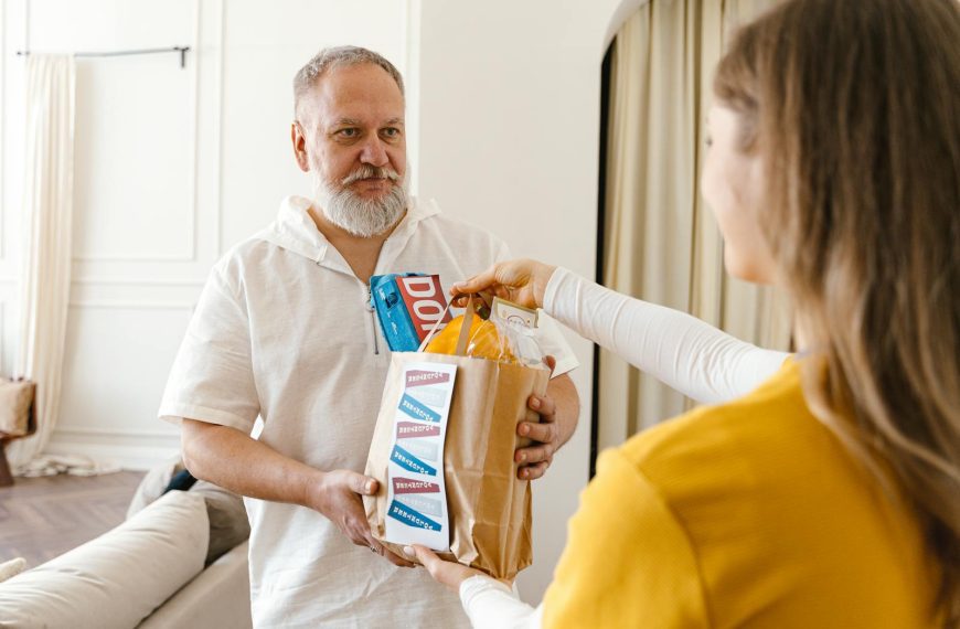 An elderly man with a beard receiving a donation in a paper bag indoors, highlighting community support.