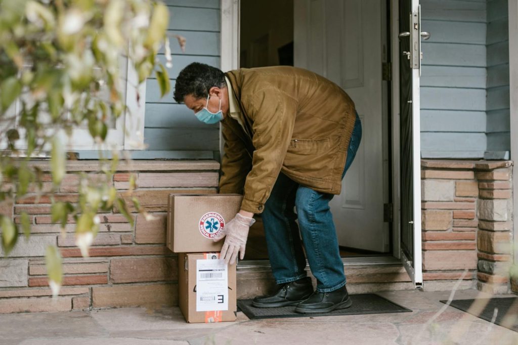 Man wearing mask delivering packages to doorstep for contactless COVID-19 safety.