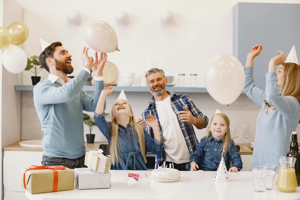 A happy family celebrating together indoors with balloons, cake, and gifts.