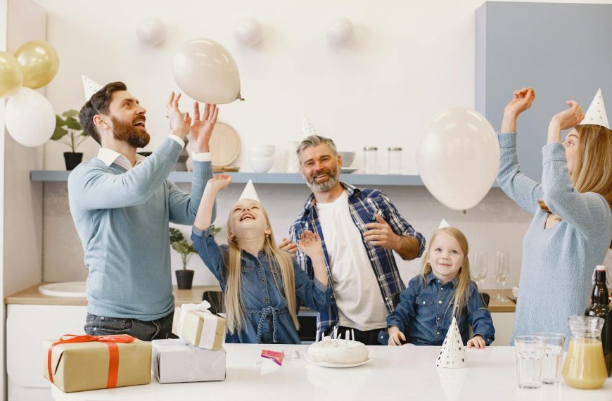 A happy family celebrating together indoors with balloons, cake, and gifts.