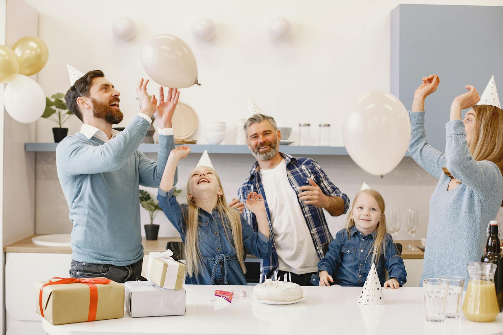 A happy family celebrating together indoors with balloons, cake, and gifts.