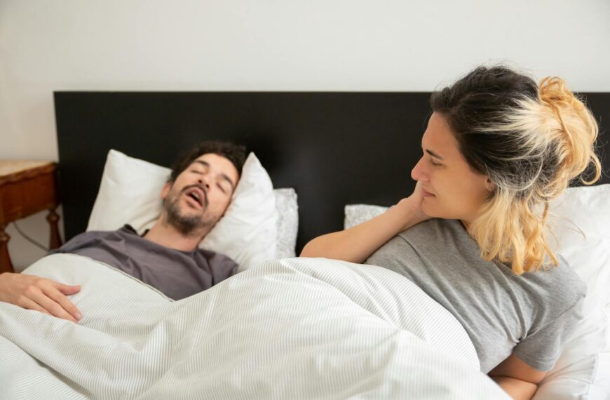 A couple in bed with a man snoring loudly and a woman looking restless on her pillow.