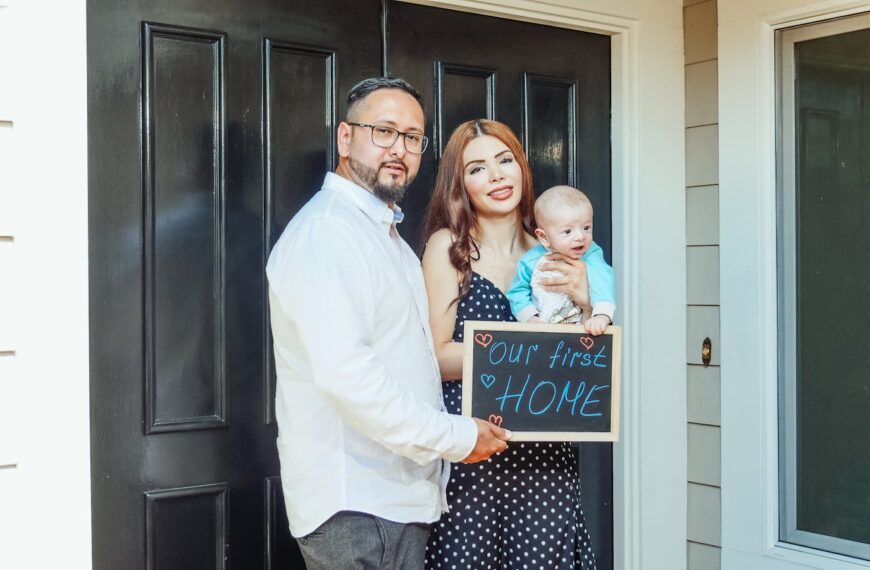 Young family with baby holding a sign 'Our First Home' at doorstep, symbolizing new beginnings.