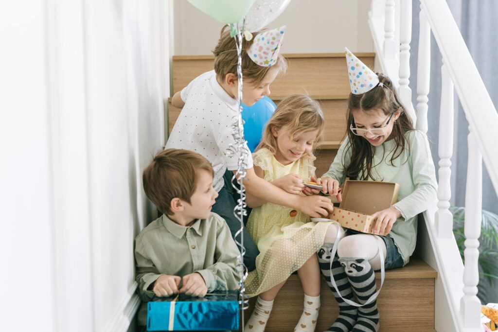 Children enjoying a birthday party with gifts and balloons, captured indoors on a staircase.
