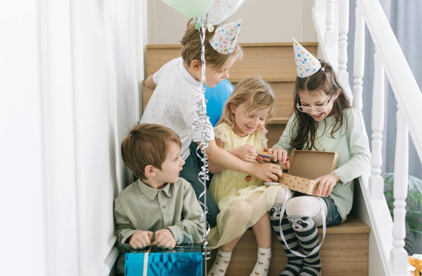Children enjoying a birthday party with gifts and balloons, captured indoors on a staircase.