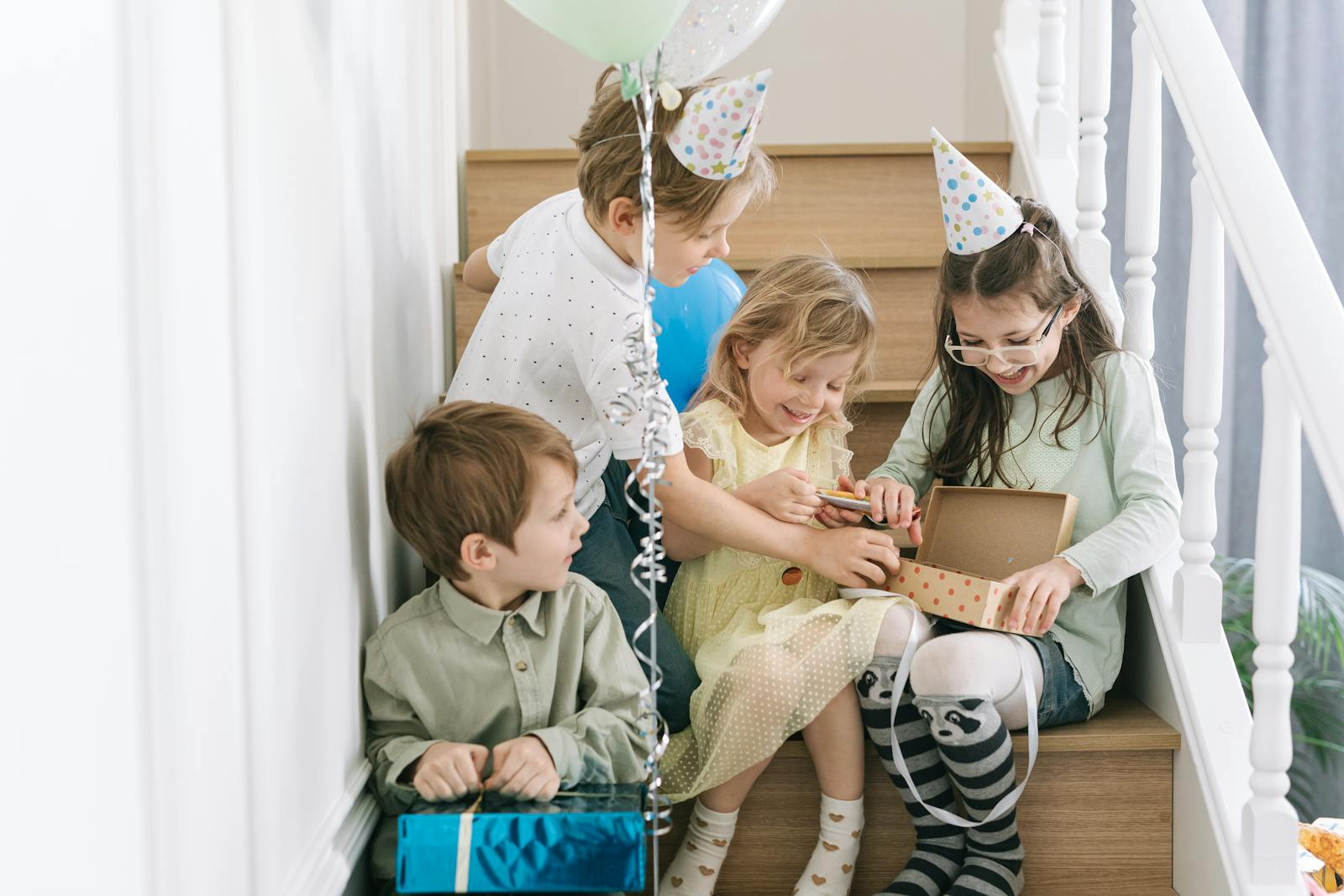 Children enjoying a birthday party with gifts and balloons, captured indoors on a staircase.