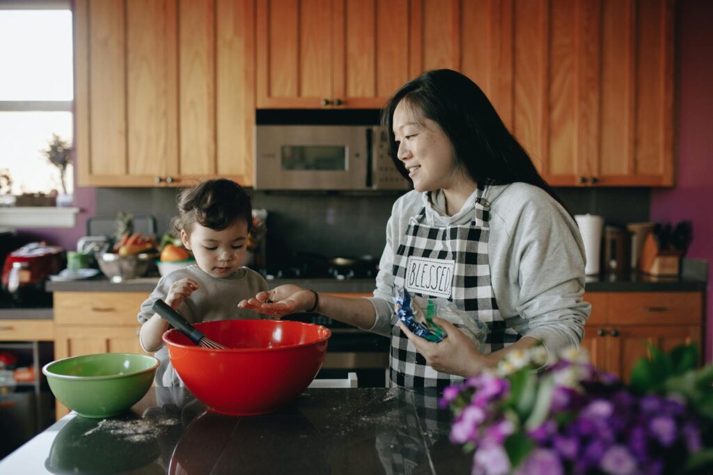 A mother and daughter share a joyful moment baking together in a bright kitchen.