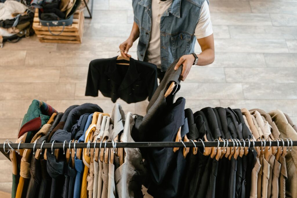 A person holds a jacket while organizing clothes on a rack in a stylish boutique.