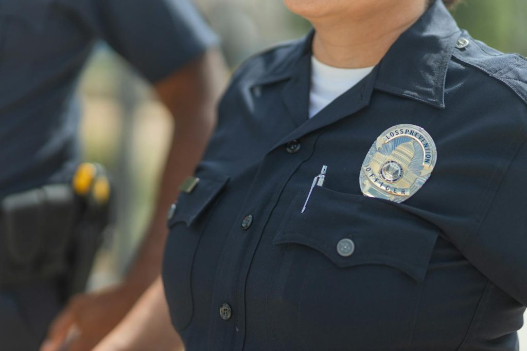 Close-up of police officers in uniform, displaying badge and radio outdoors.