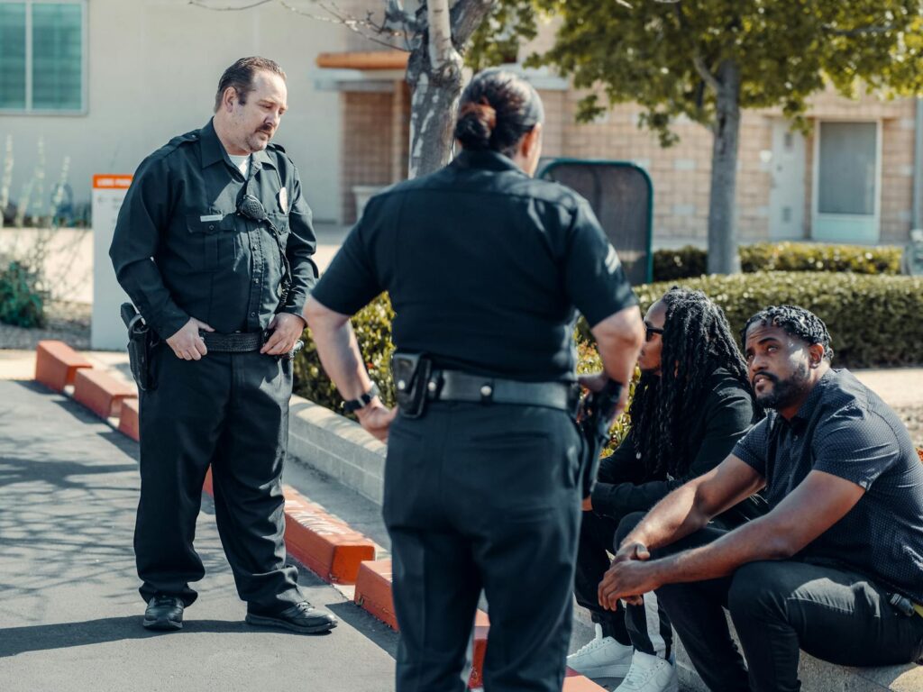 Police officers interacting with seated individuals in an urban outdoor setting.