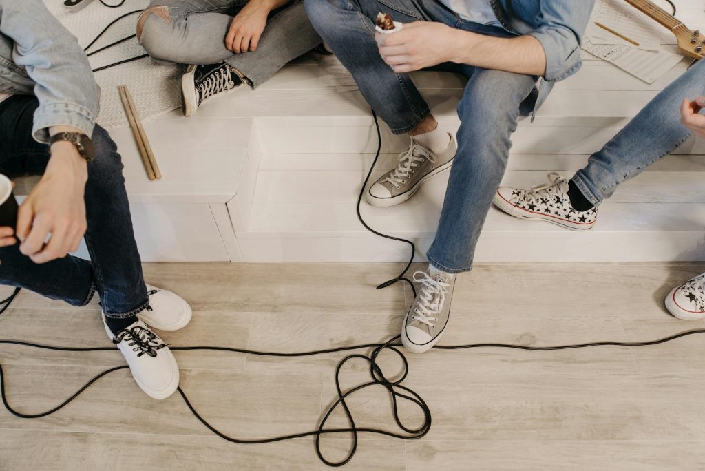 Group of young adults sitting together with musical cables and instruments in a casual setting.