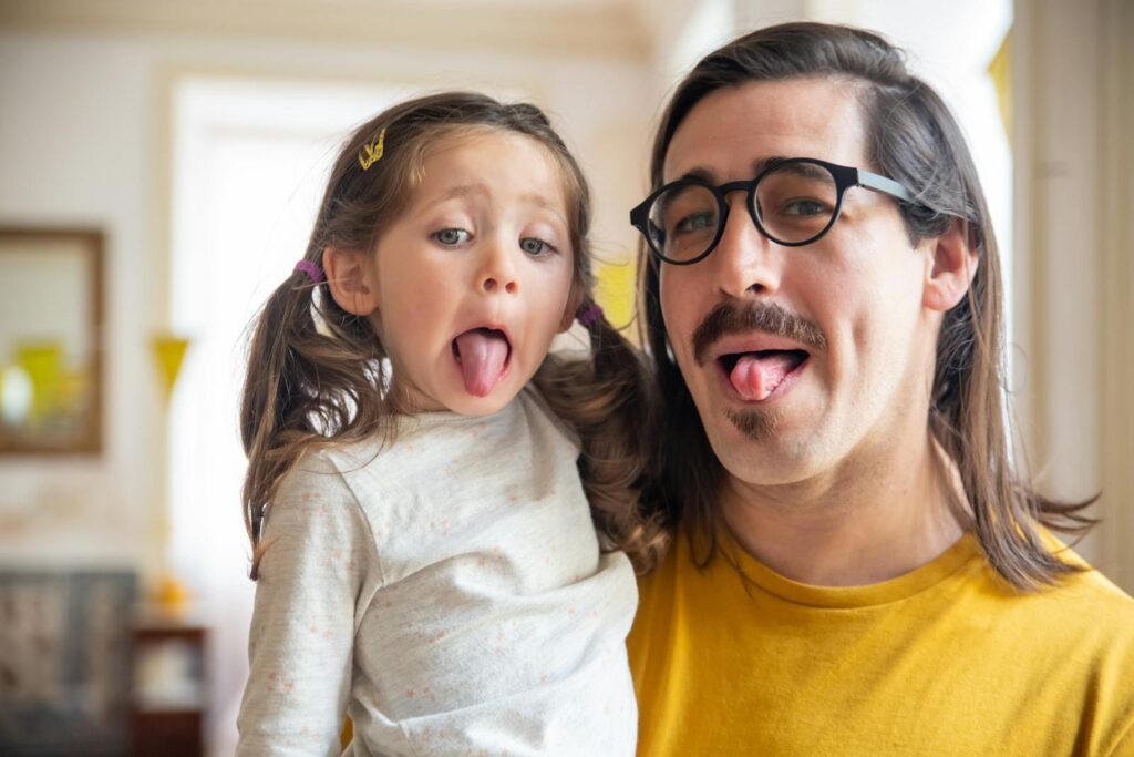 A fun moment between a father and daughter as they stick their tongues out playfully.