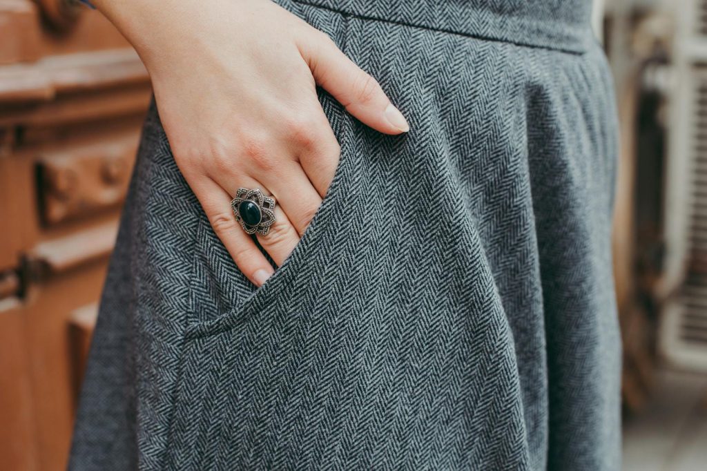 Close-up of a woman's hand with a vintage ring resting on blue tweed fabric, showcasing elegant fashion.