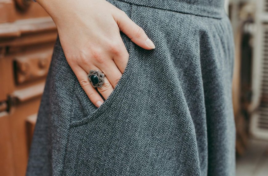Close-up of a woman's hand with a vintage ring resting on blue tweed fabric, showcasing elegant fashion.