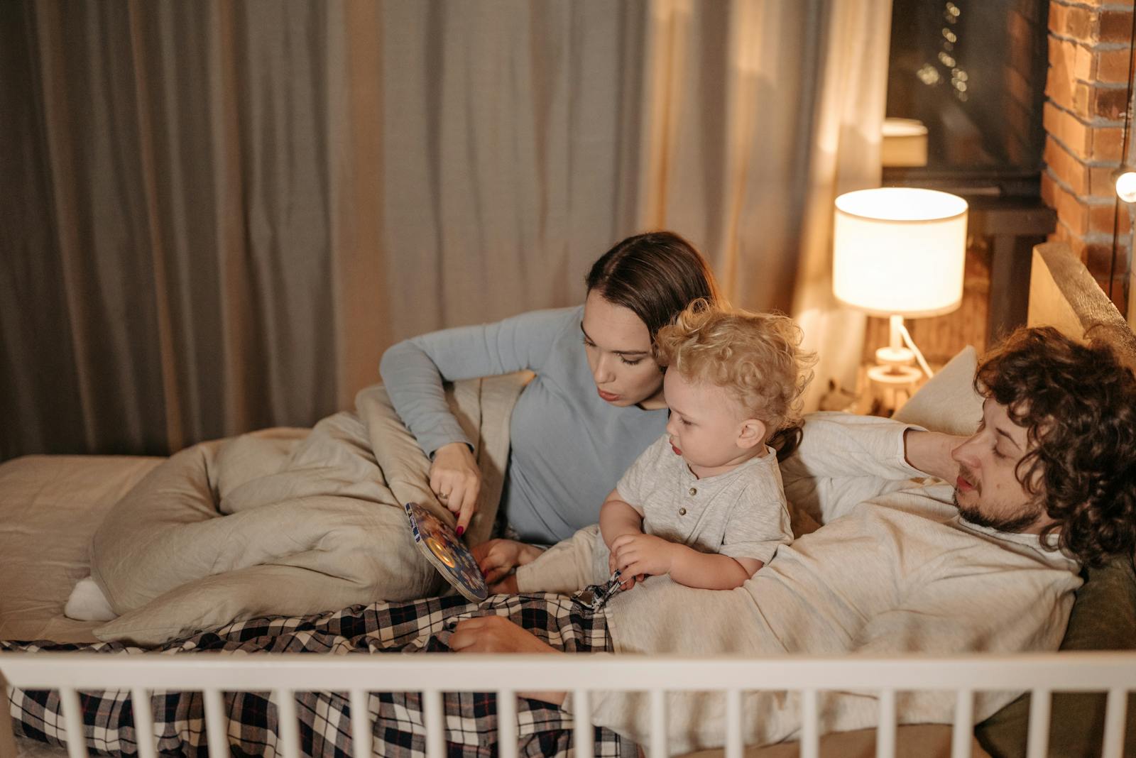 Father and mother reading to their child in bed during nighttime for a cozy bedtime story.