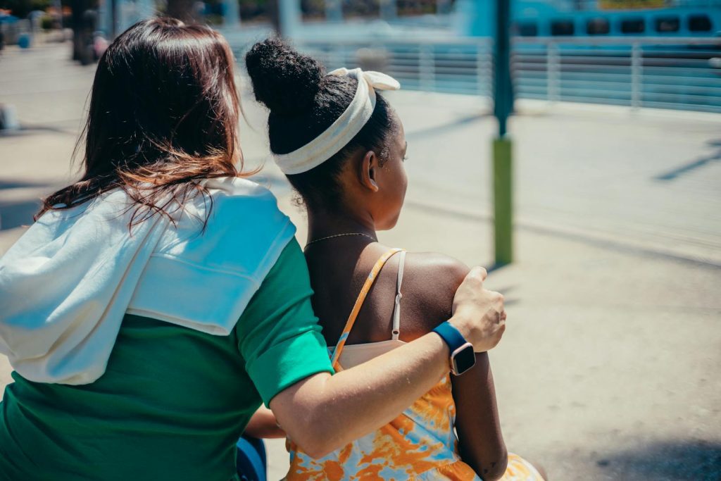 A mother and daughter share a tender moment outdoors on a sunny day.