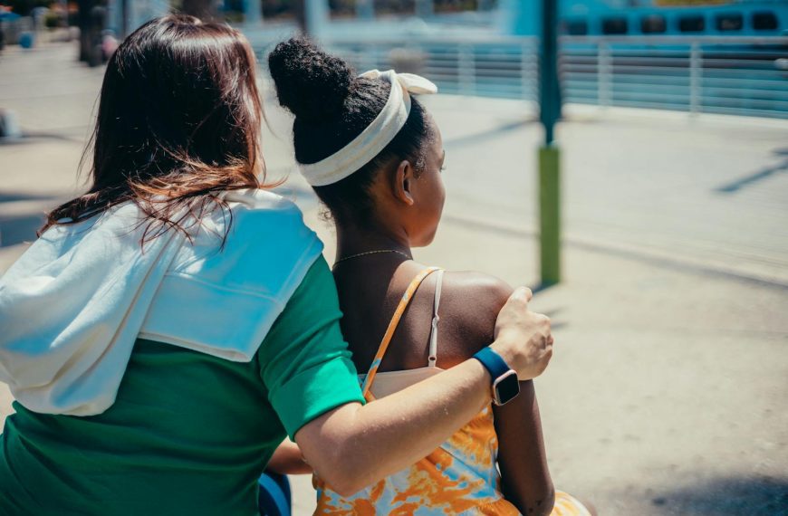 A mother and daughter share a tender moment outdoors on a sunny day.