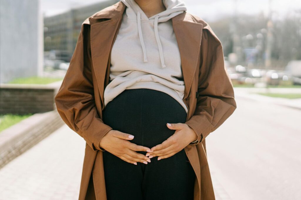 A stylish pregnant woman with hands on her belly in a modern urban environment.