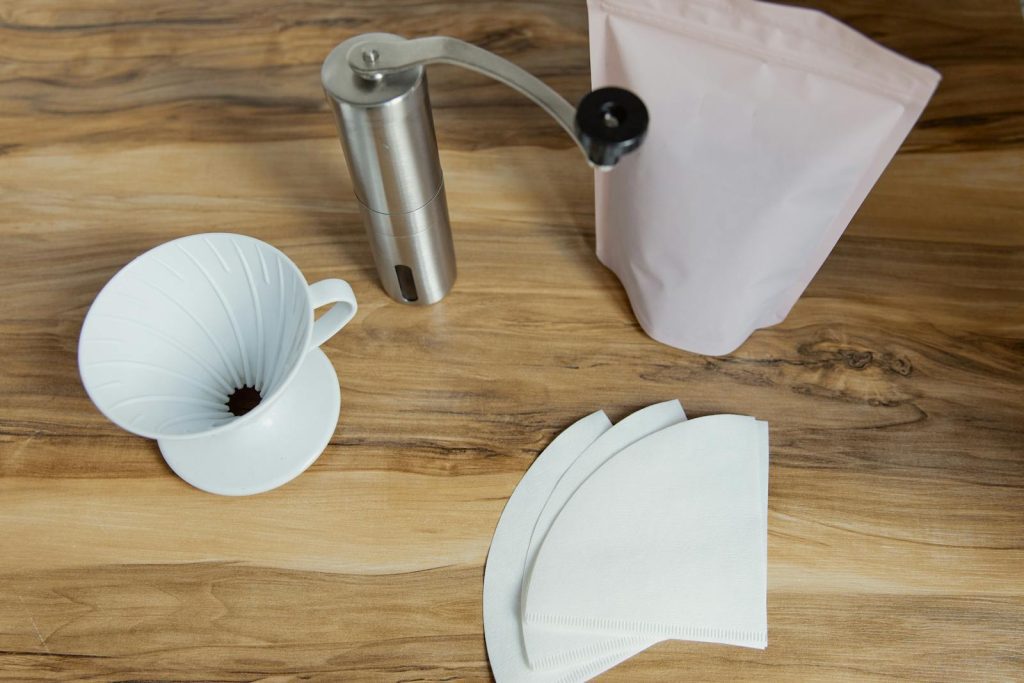 A wooden table with coffee filters, a grinder, and a coffee dripper for making fresh coffee.