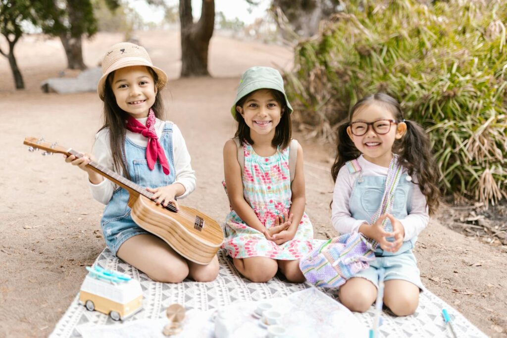 Three smiling girls enjoying a cheerful picnic on a sunny day outdoors.