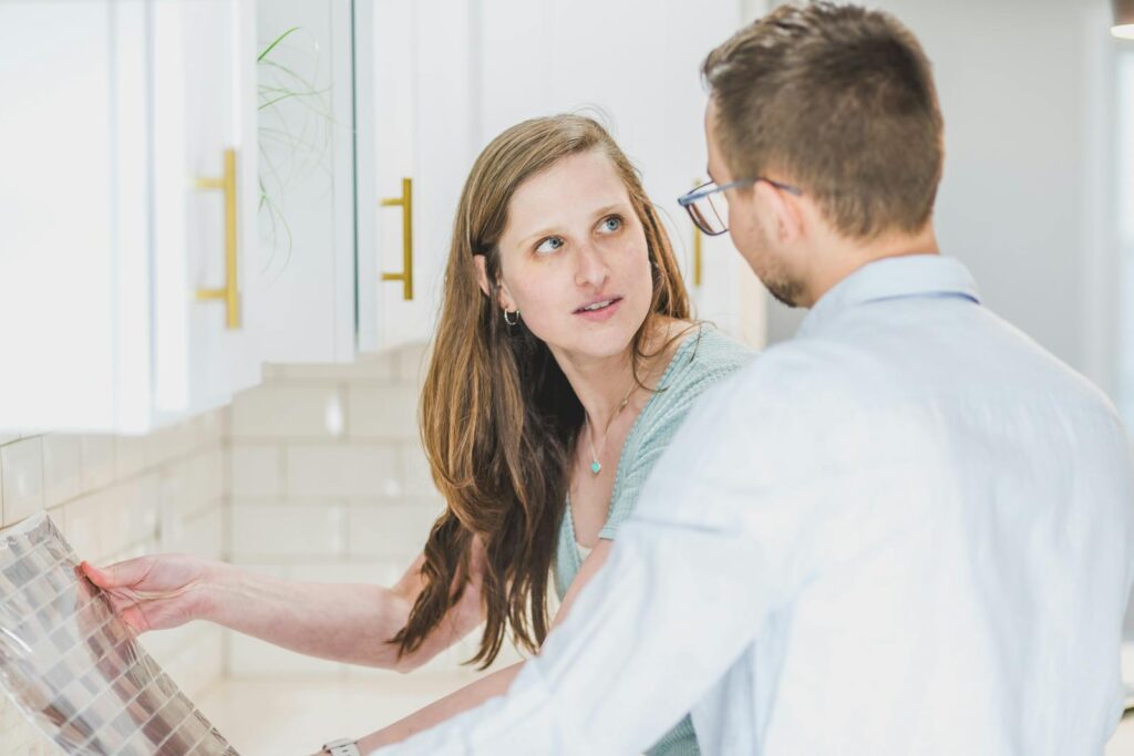 Young couple in bright kitchen discussing ideas for tile backsplash renovation.