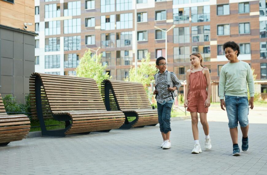 Three children of diverse backgrounds walking and chatting in an urban school setting.