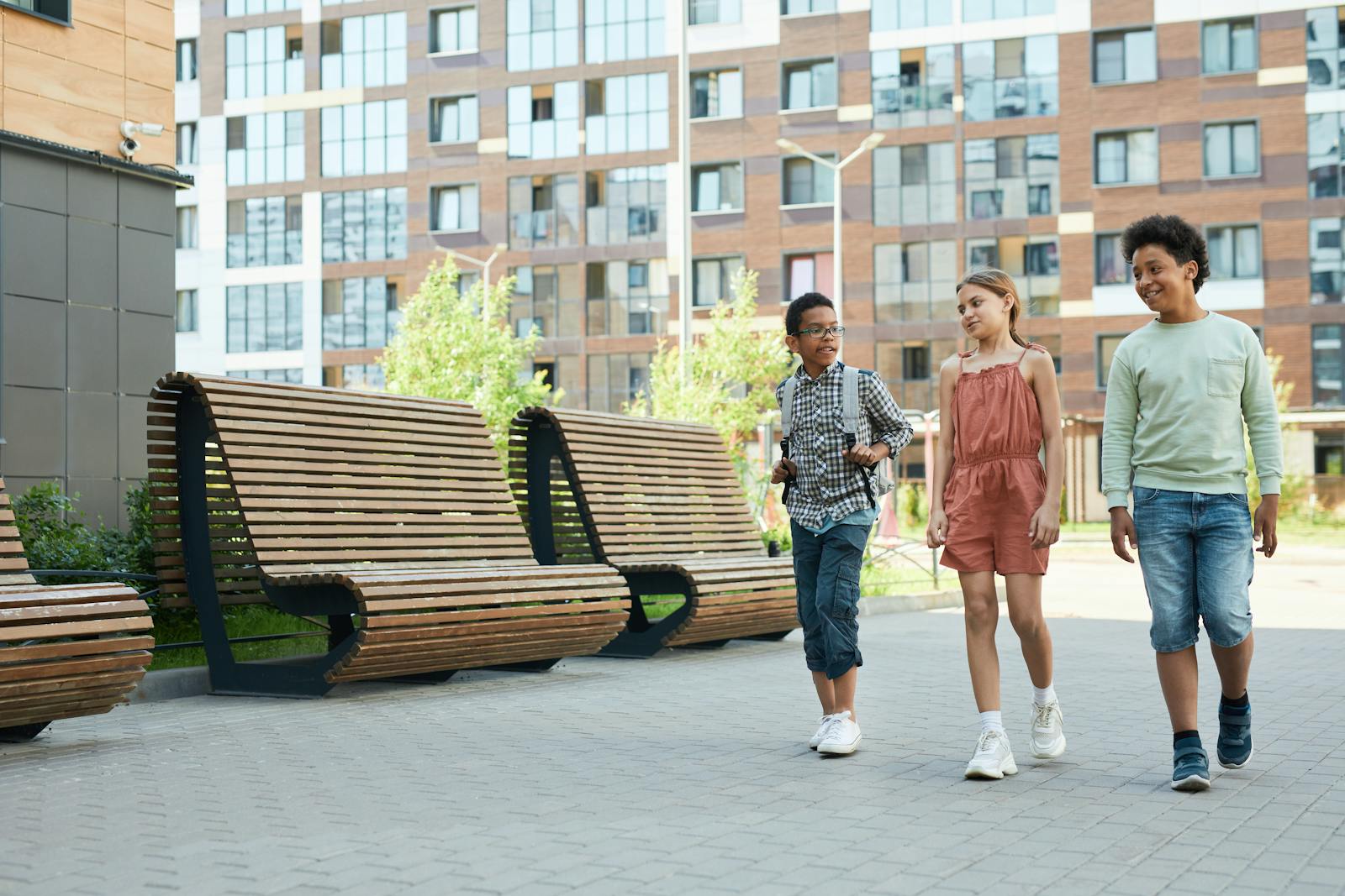 Three children of diverse backgrounds walking and chatting in an urban school setting.