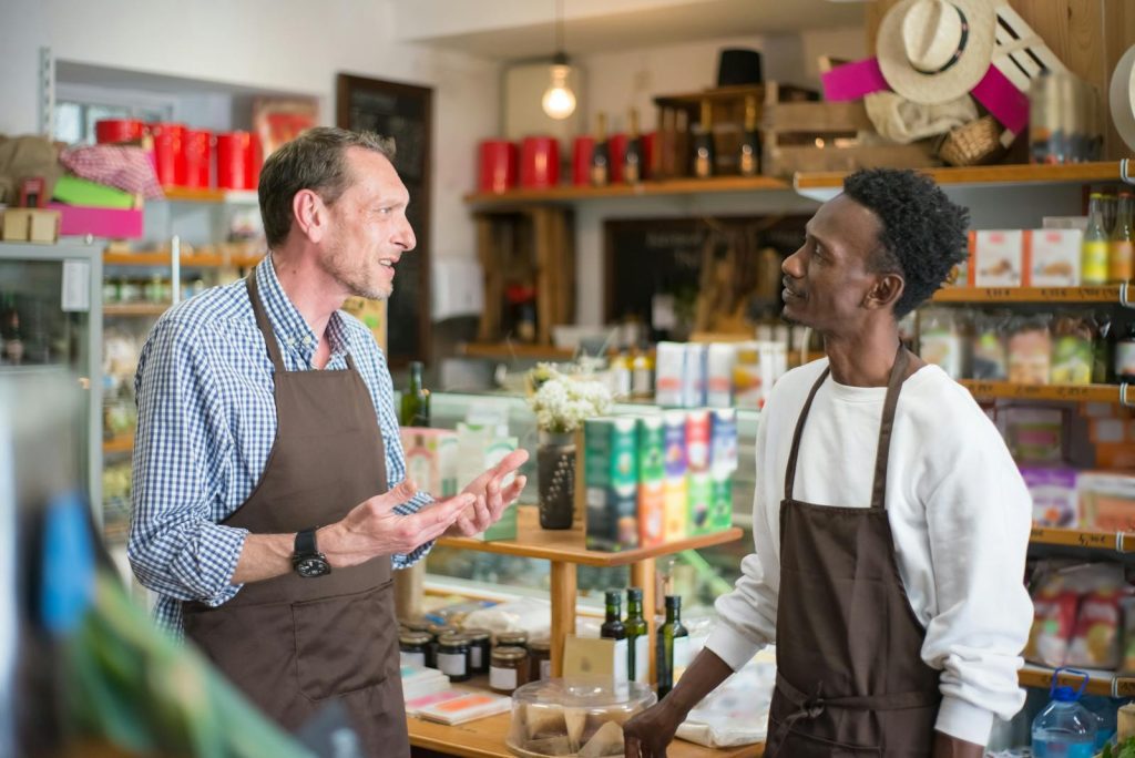 Two colleagues in aprons conversing in a grocery store setting.