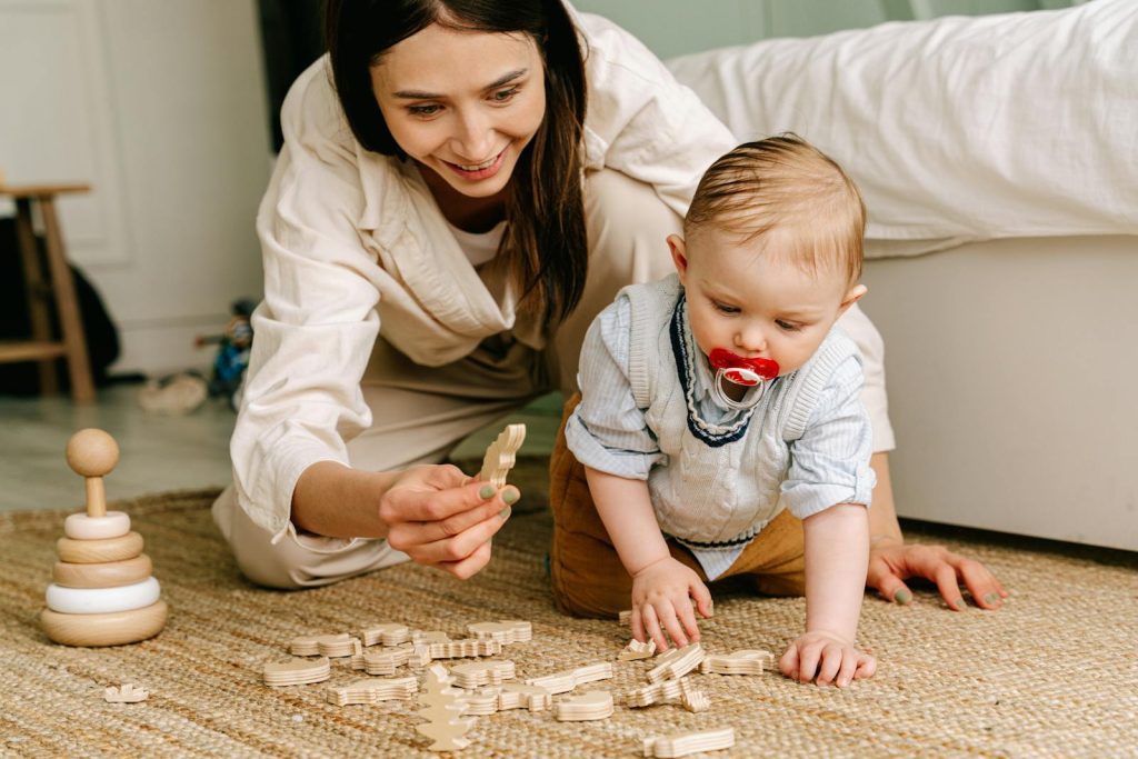 A mother and baby enjoying playtime indoors with wooden toys on the floor.
