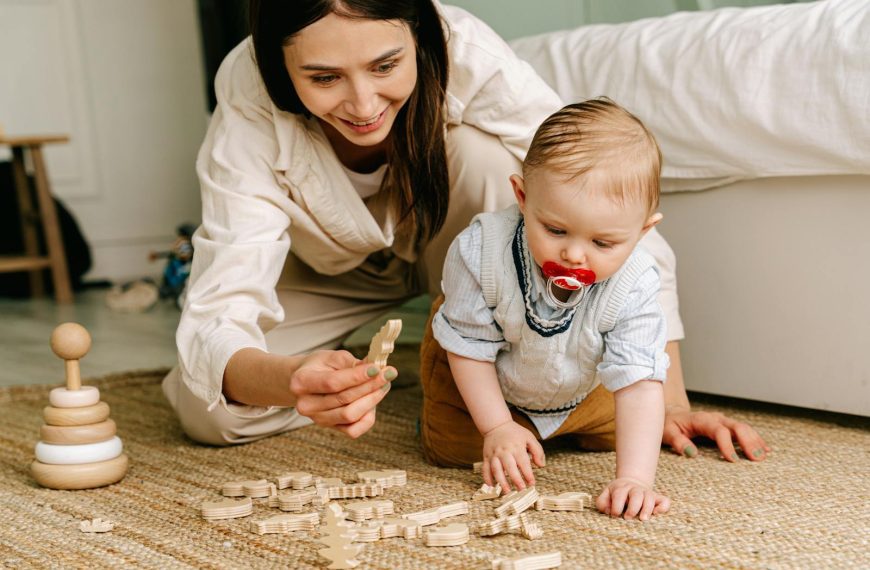 A mother and baby enjoying playtime indoors with wooden toys on the floor.