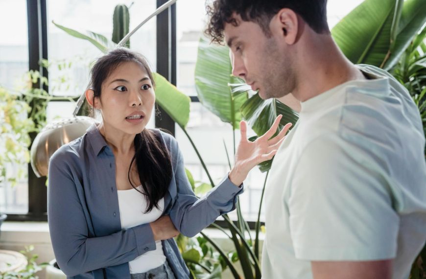 A couple engaged in a heated discussion indoors surrounded by plants, expressing emotions.