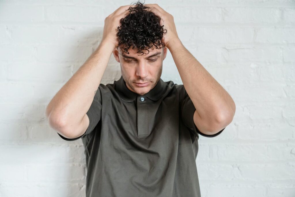 Portrait of a curly haired man looking down in thought against a white background.