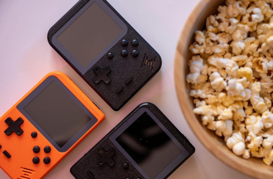 Close-up of retro handheld game consoles and popcorn, perfect for gaming nights.