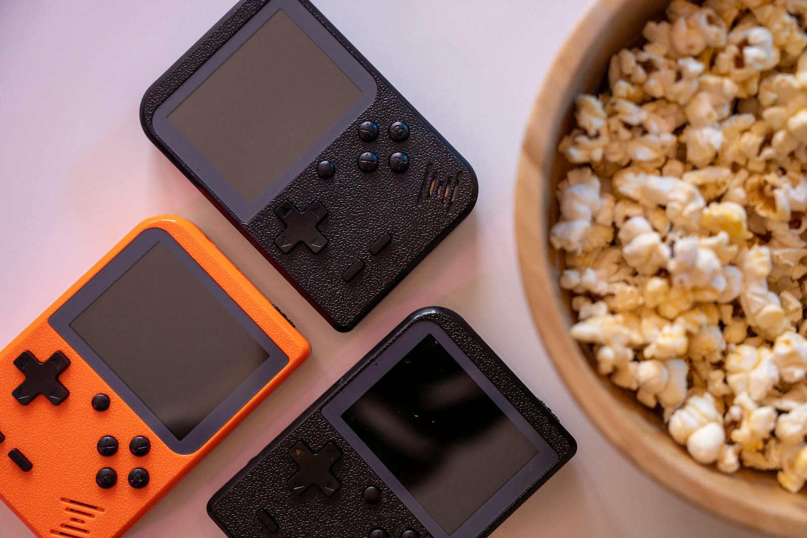 Close-up of retro handheld game consoles and popcorn, perfect for gaming nights.