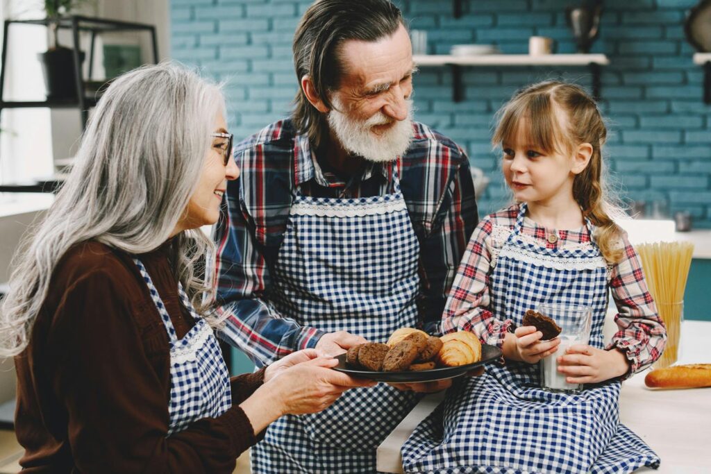 Joyful elderly couple baking and sharing cookies with their granddaughter in a cozy kitchen.