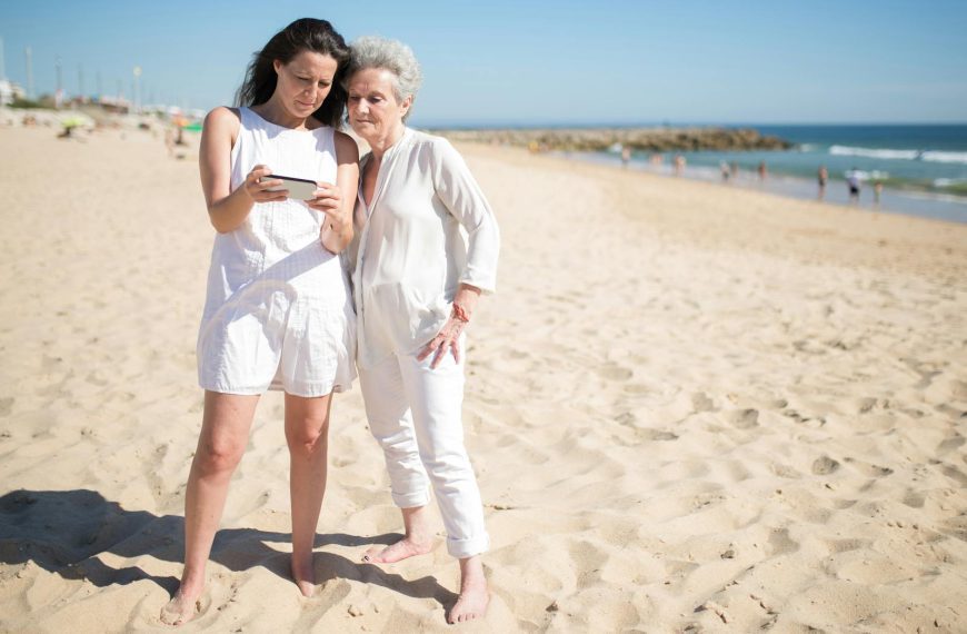 Mother and daughter enjoying a sunny day at a Portuguese beach, sharing moments on a smartphone.