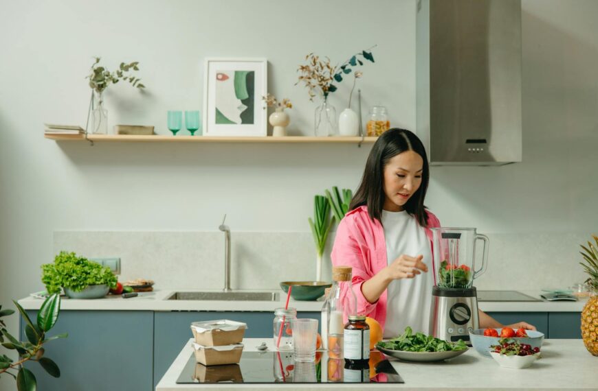 Asian woman blending fresh fruits and vegetables in a stylish kitchen setting.