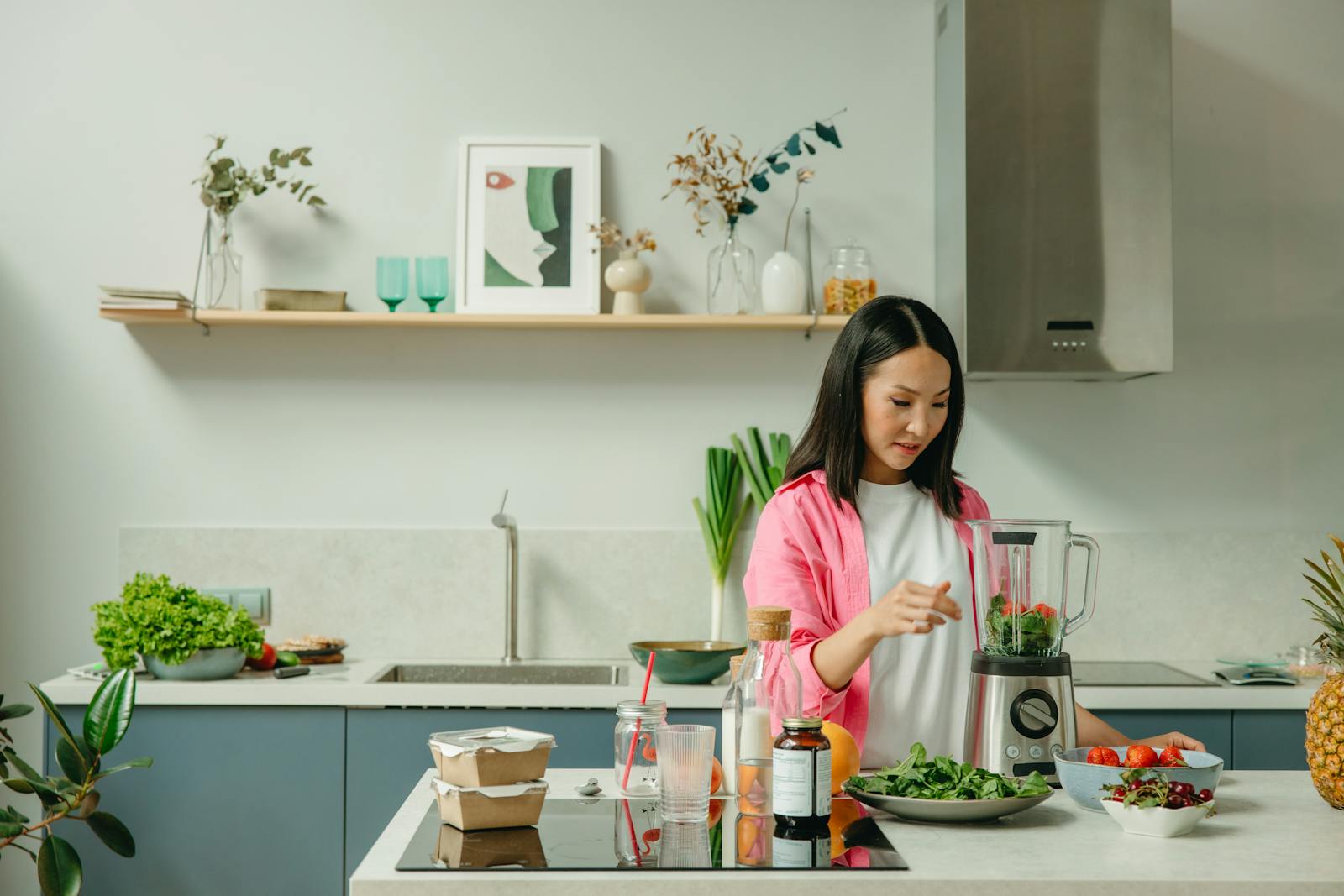 Asian woman blending fresh fruits and vegetables in a stylish kitchen setting.