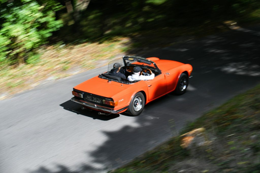 Orange convertible driving on a tree-lined road.