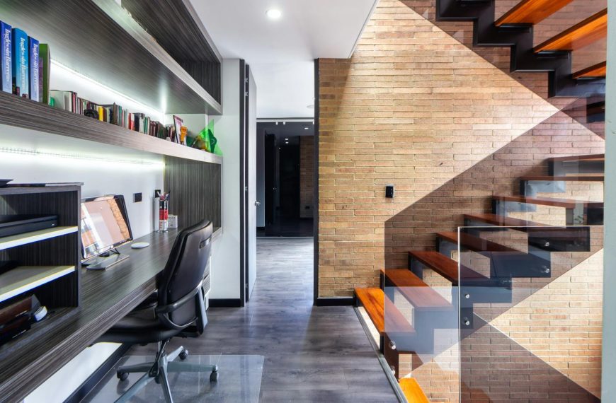Contemporary office space featuring a sleek desk, modern design, and wooden staircase.