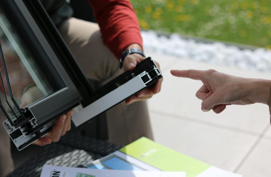 Close-up of two people examining an aluminum window frame outdoors.