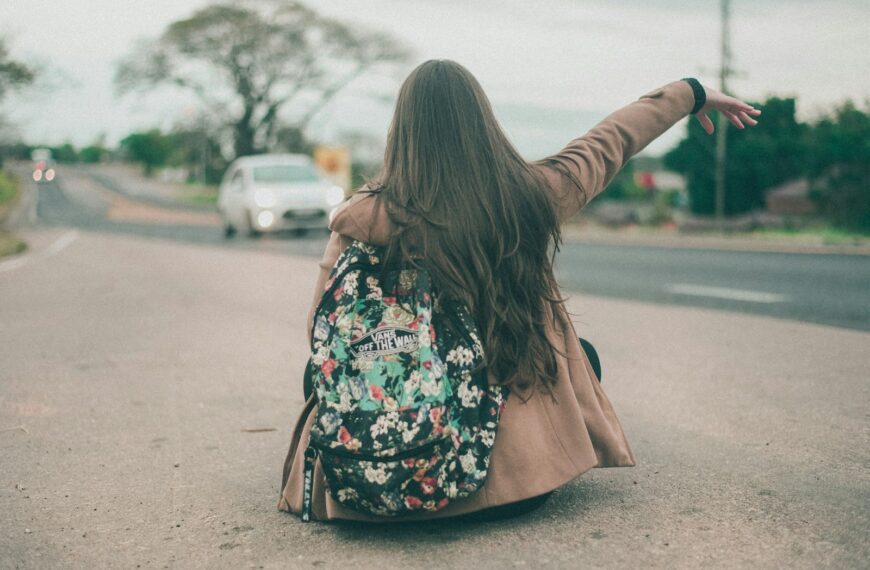 woman sitting and raising right hand on concrete pathway near road