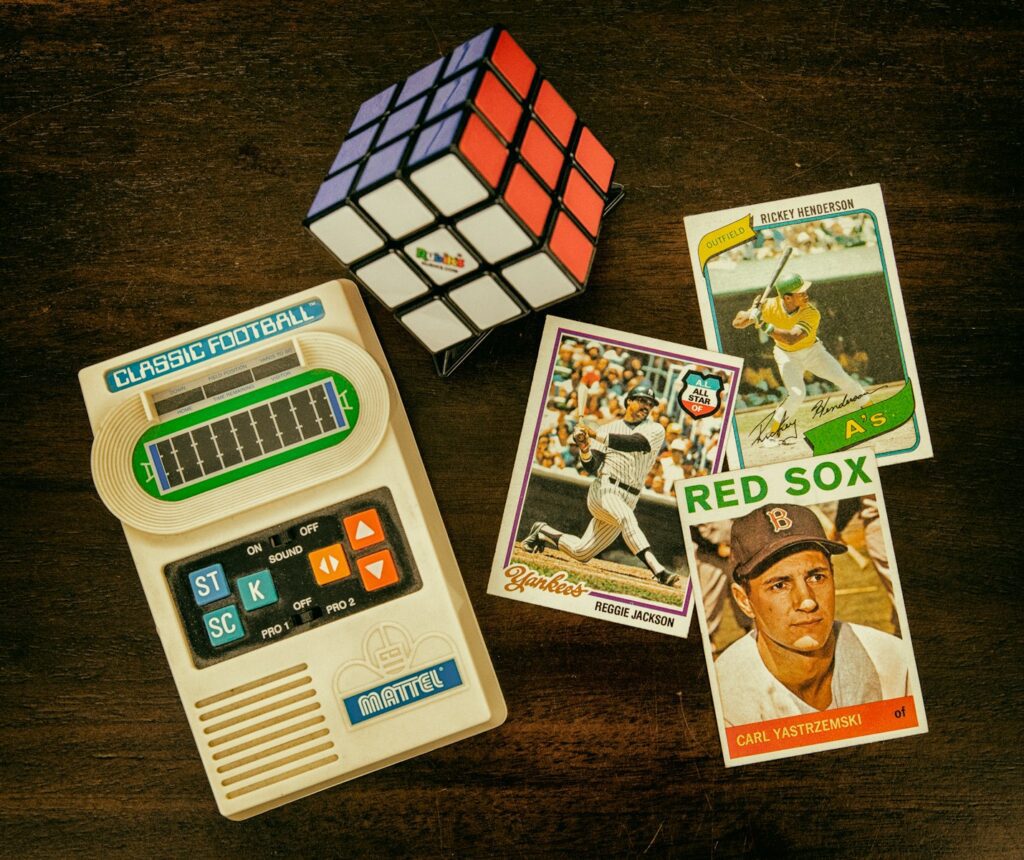 three baseball trading cards beside Rubik's cube and Classic Football handheld game console
