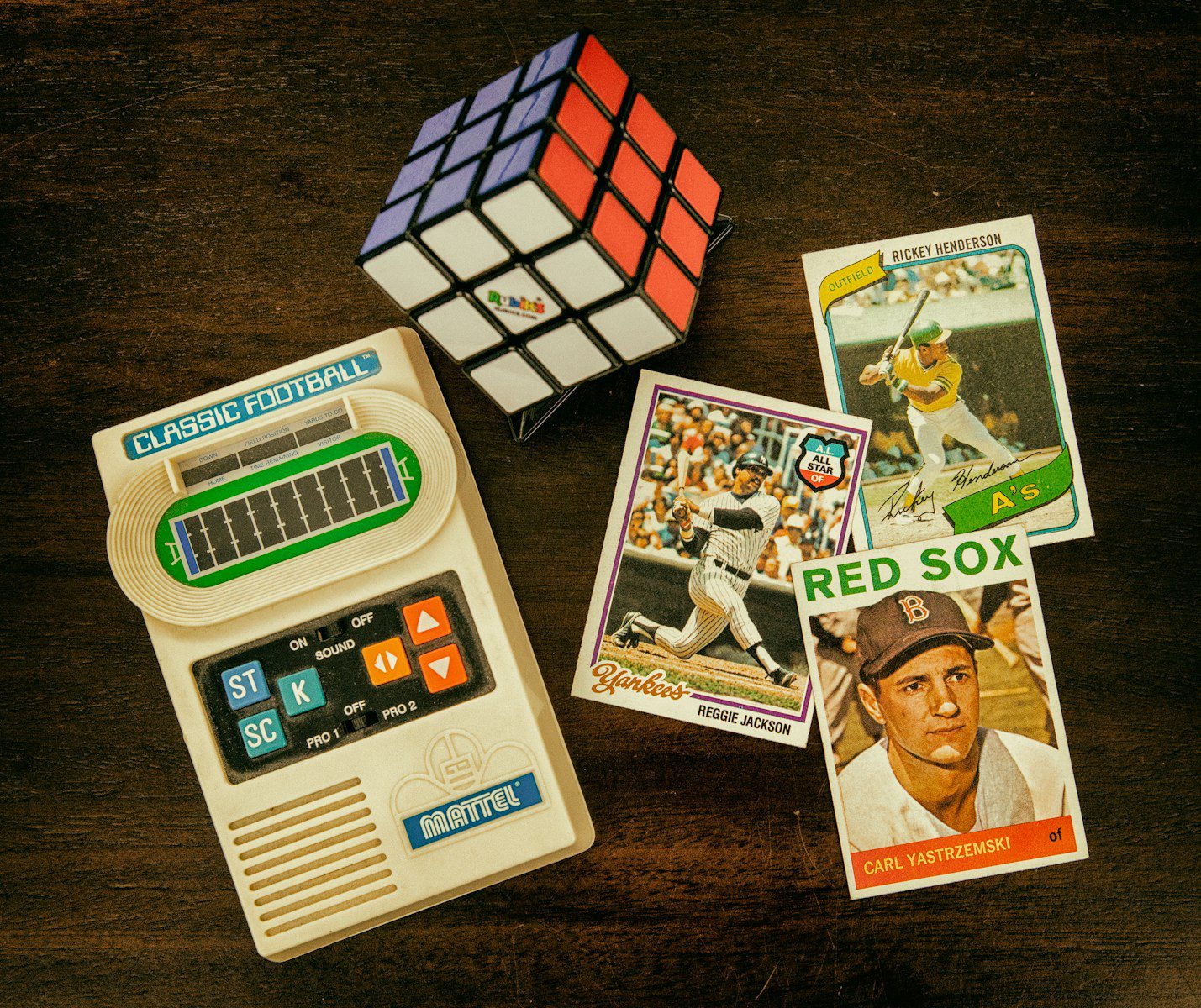 three baseball trading cards beside Rubik's cube and Classic Football handheld game console