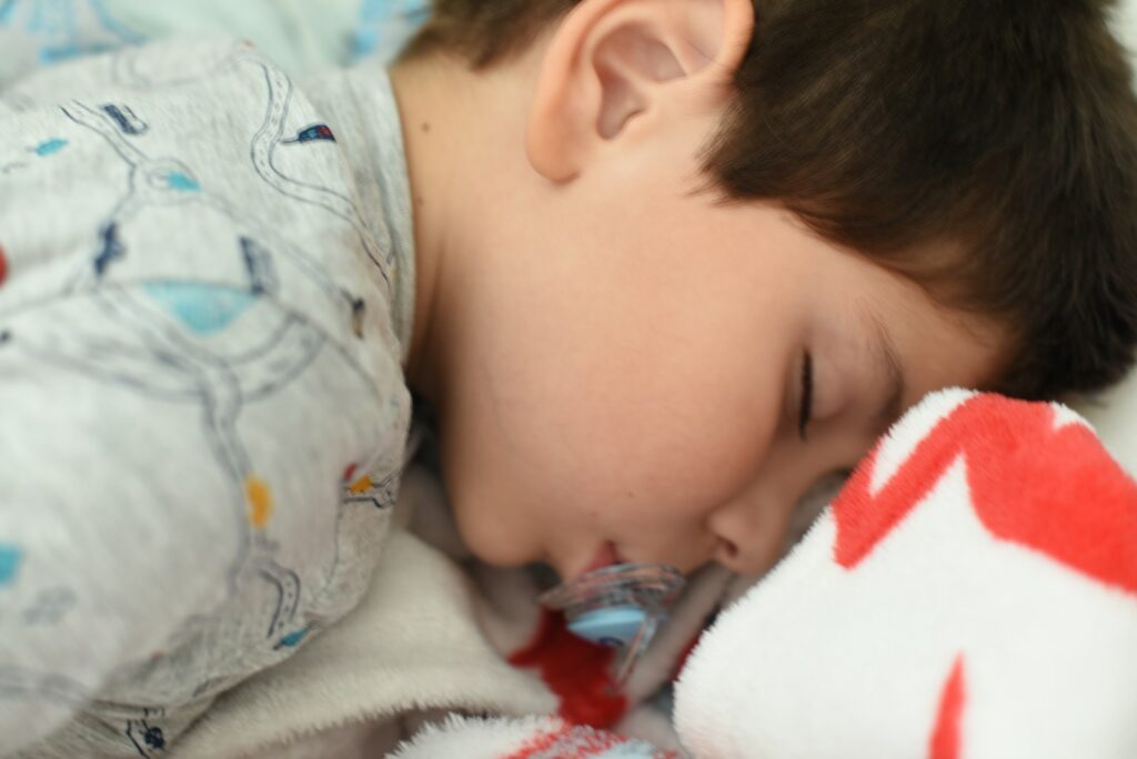 a young boy sleeping on a bed with a stuffed animal