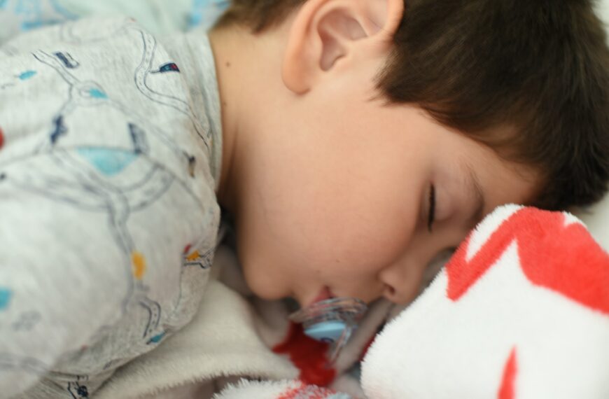 a young boy sleeping on a bed with a stuffed animal