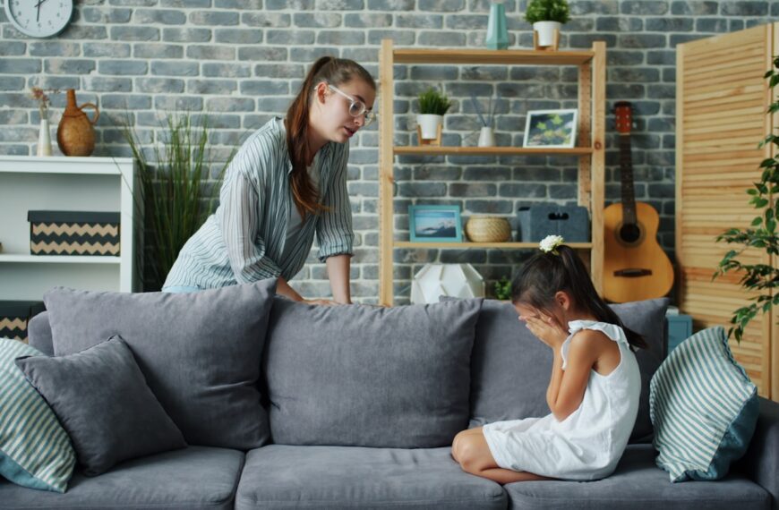 Mother scolds crying daughter on sofa in living room.