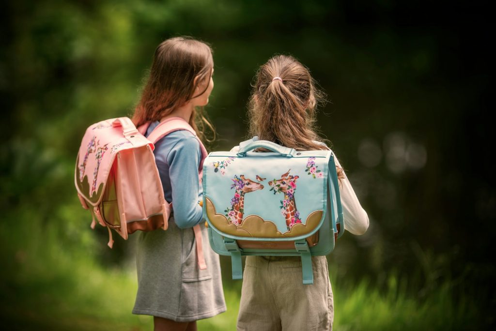 Two girls stand with their backpacks near water.